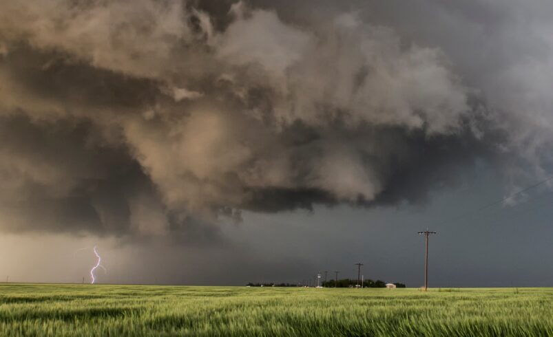 Storm clouds loom over a green field with lightning striking.